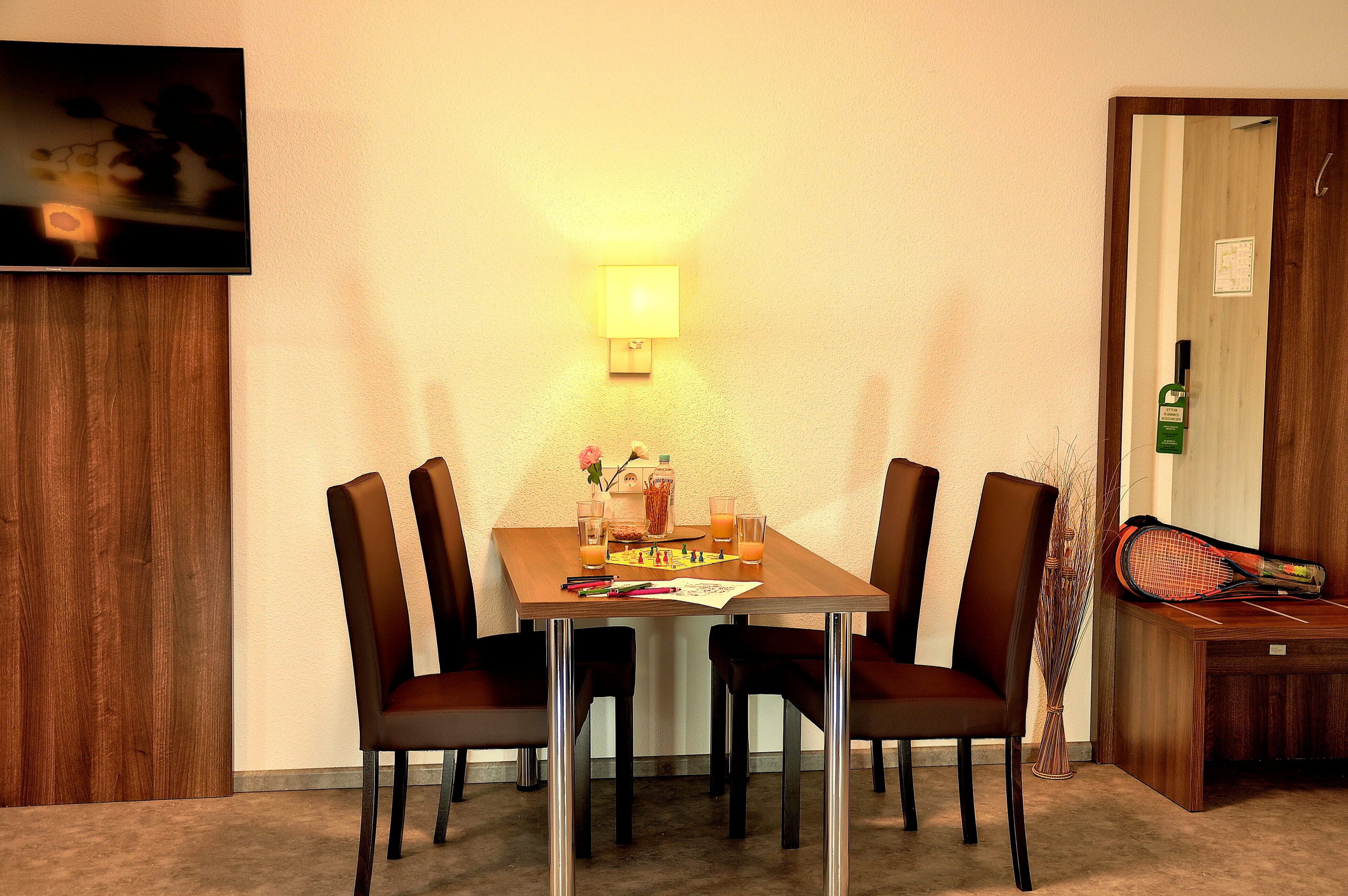 Ein Essbereich mit Holztisch, vier Stühlen, einem an der Wand montierten Fernseher und einer Tischlampe.
