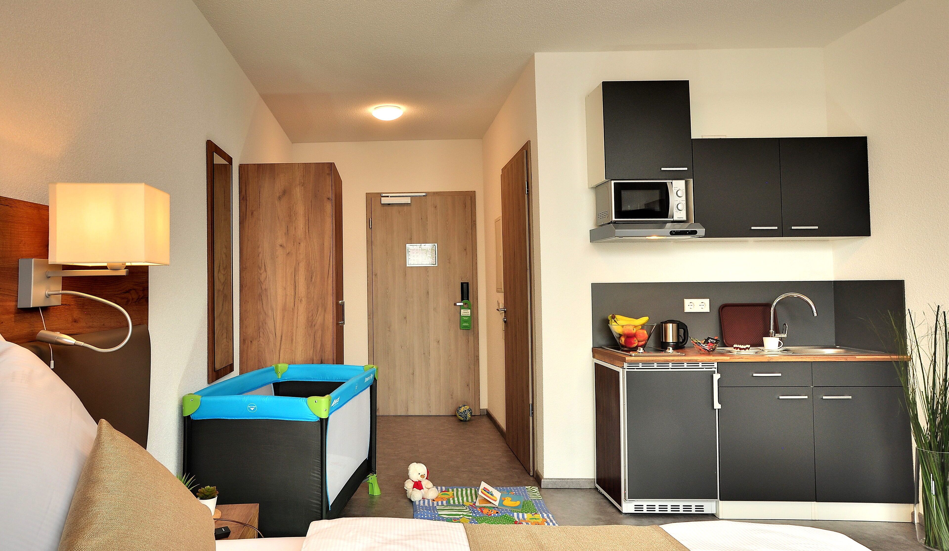 A compact hotel room with a kitchenette, a small play area, and a bed.