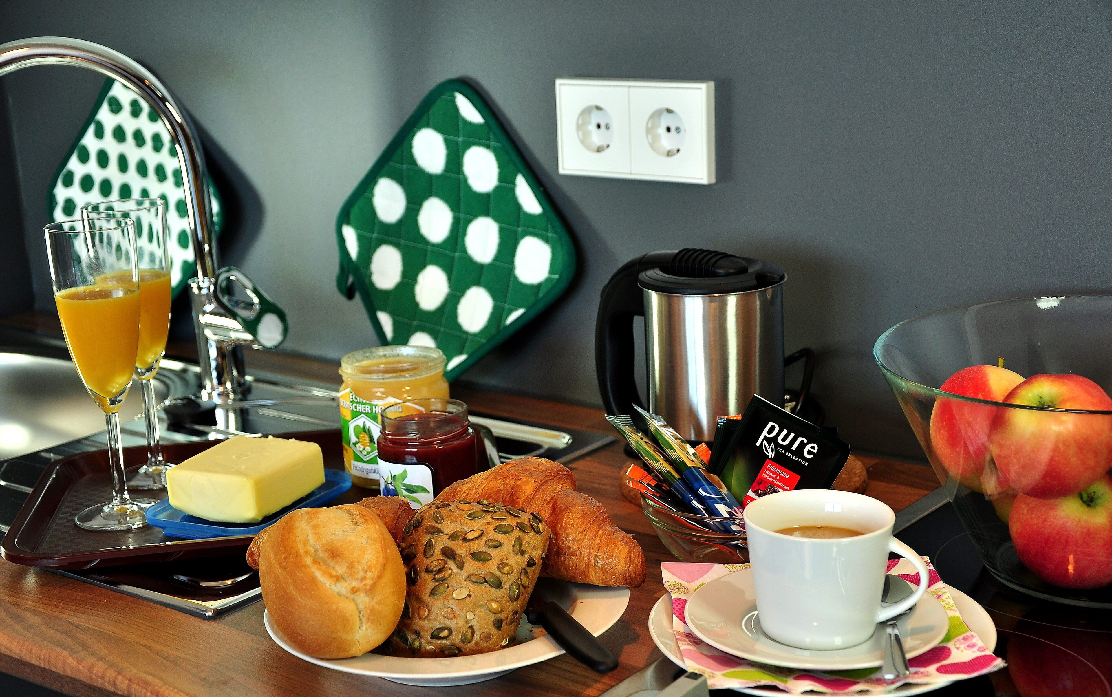 A breakfast setup with croissants, bread, butter, jam, coffee, and apples.