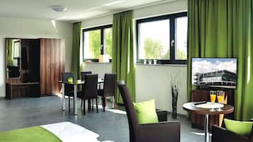 A hotel room with a bed, a TV, a dining area with chairs and a table, and a window with curtains.