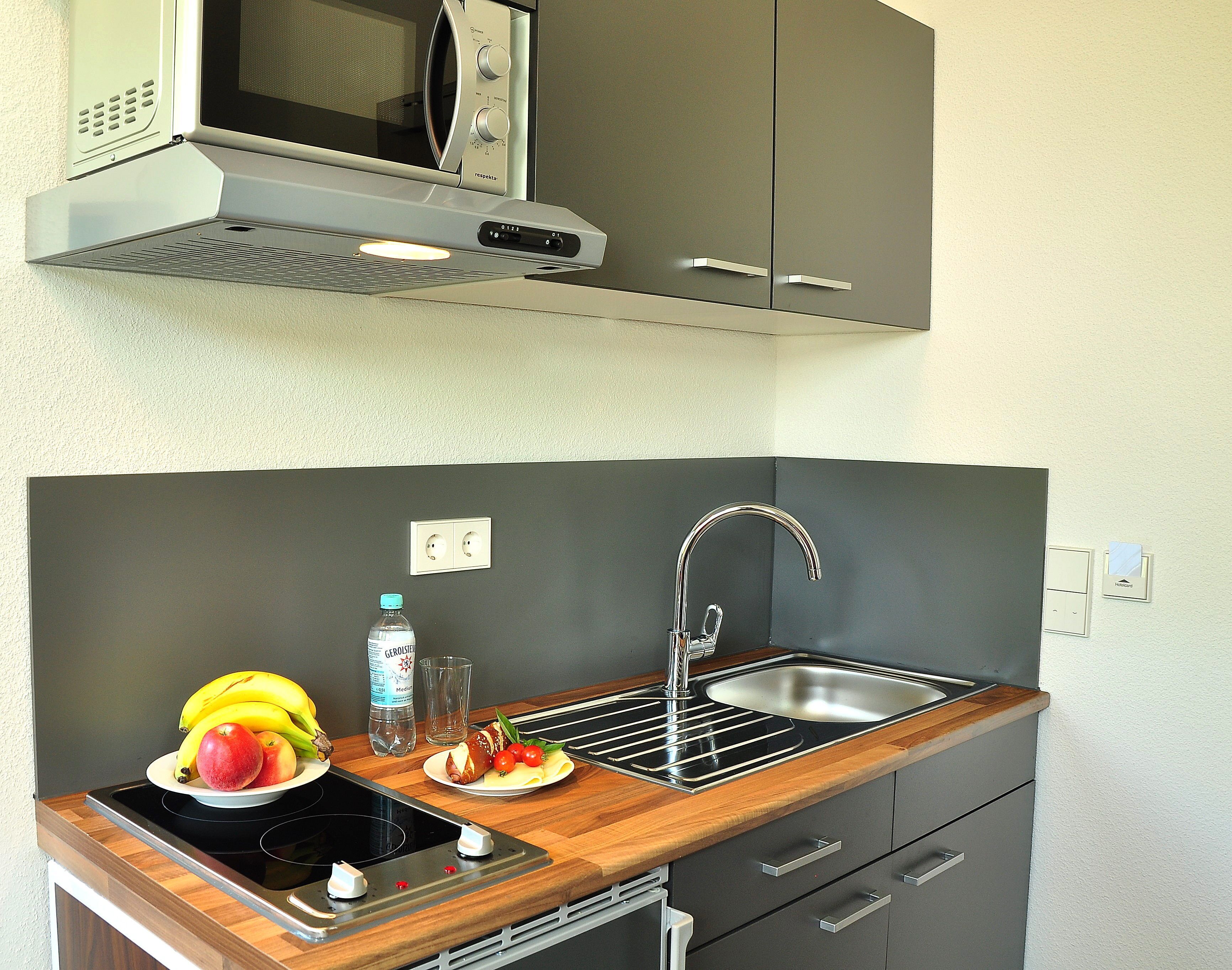 A compact kitchen with a microwave, sink, and wooden countertop.