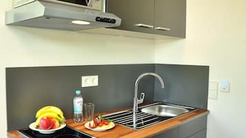 A compact kitchen with a microwave, sink, and wooden countertop.