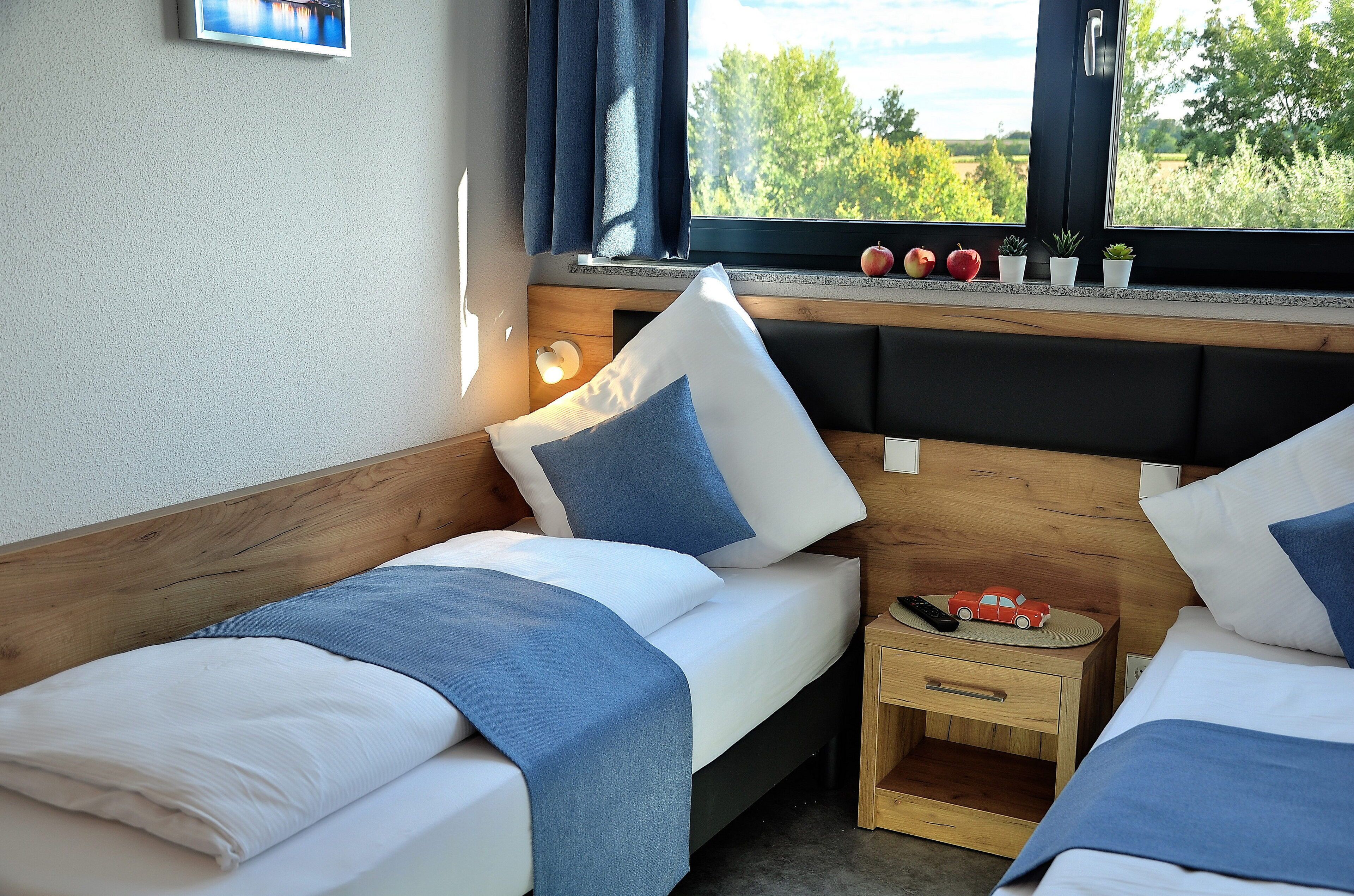 A bedroom with two beds, a nightstand, and a window with a view of greenery.