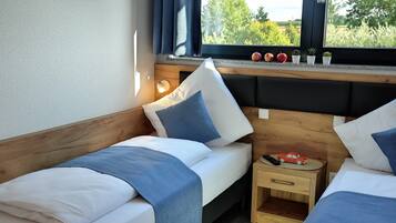 A bedroom with two beds, a nightstand, and a window with a view of greenery.
