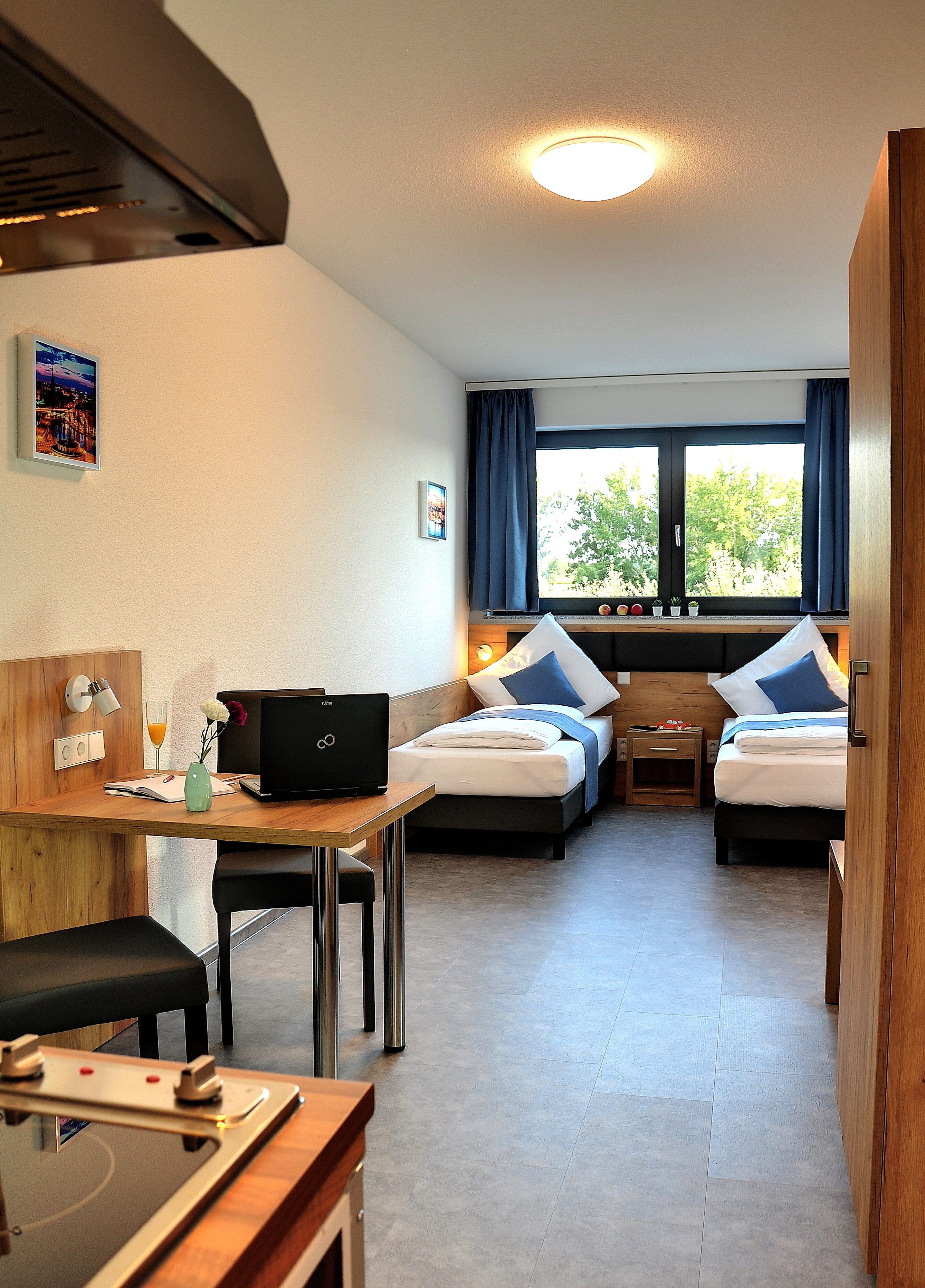 Camera d'albergo compatta con un letto, una scrivania e angolo cottura.