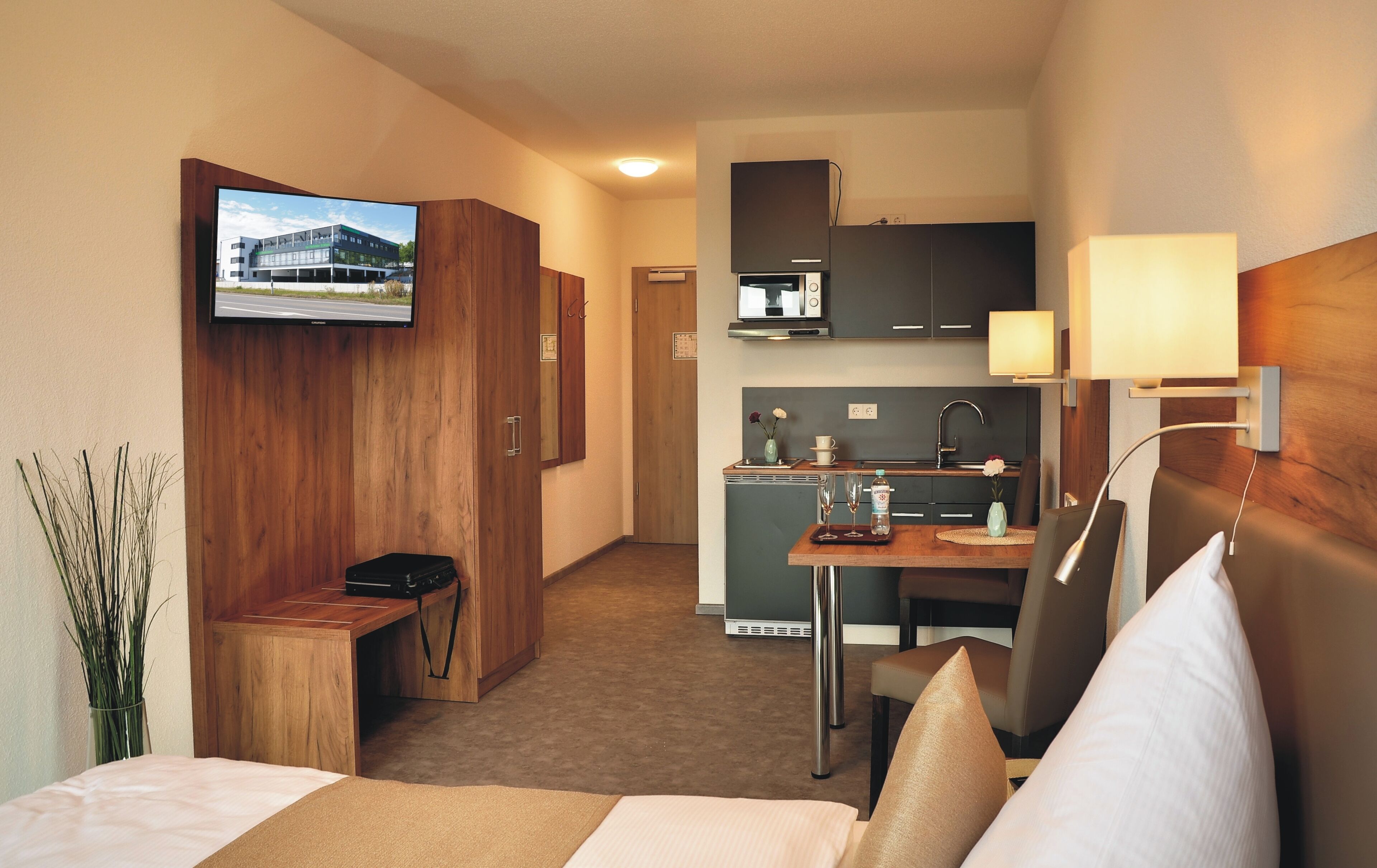Hotelkamer met een bed, bureau, televisie aan de muur, kitchenette en badkamer.
