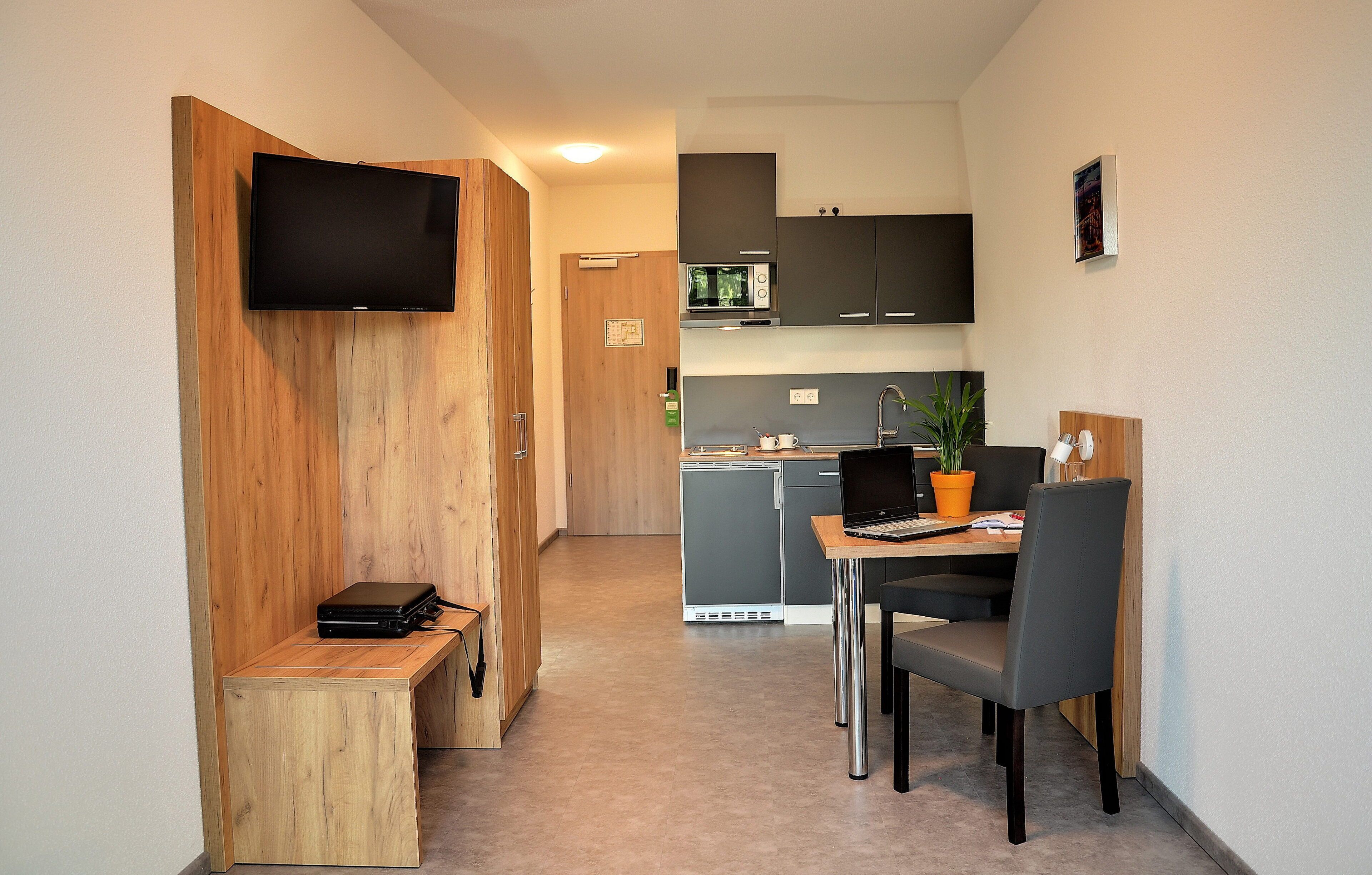 A compact kitchen with a microwave, a small refrigerator, and a wooden bench.