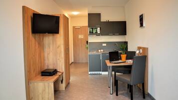 A compact kitchen with a microwave, a small refrigerator, and a wooden bench.