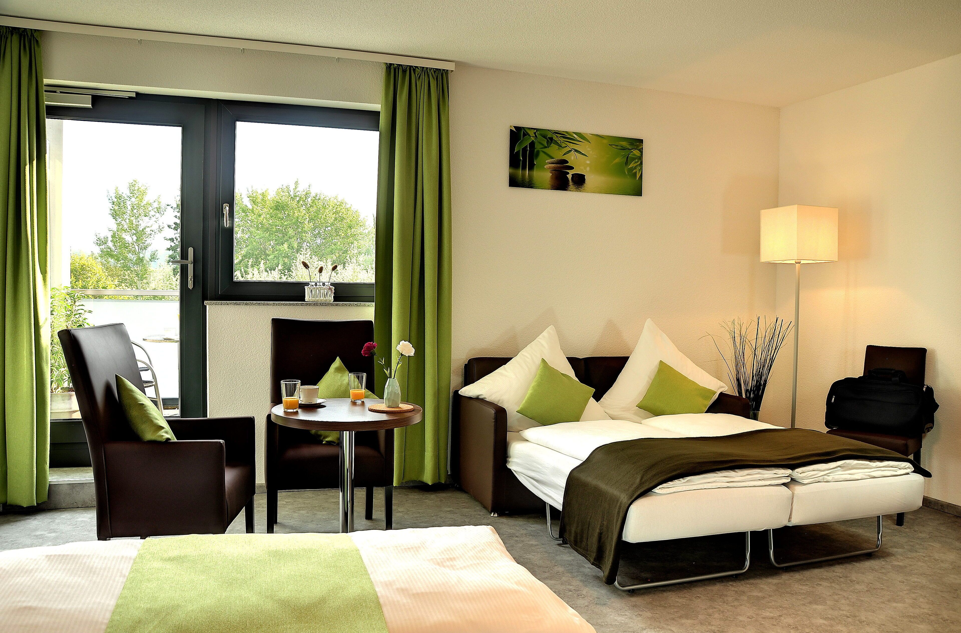 A hotel room with a bed, a desk with a chair, a sofa, and a lamp.