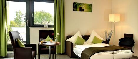 A hotel room with a bed, a desk with a chair, a sofa, and a lamp.