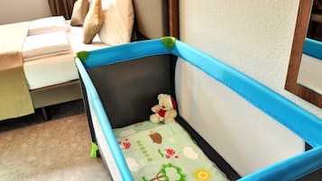Una cuna para bebé con estructura azul y colchón suave, ubicada en un rincón de una habitación con cama y ventana.