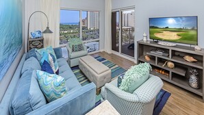 Ein modernes Wohnzimmer mit großem Fernseher, bequemen Sitzmöglichkeiten und einem Balkon mit Blick auf die Stadt.