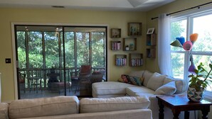 Un salon spacieux comprenant un grand canapé d’angle, une table à manger et un ventilateur de plafond. Une porte-fenêtre coulissante donne accès à un patio extérieur équipé d’une table et de chaises.