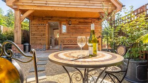 Une cabane en bois avec une table de patio, deux verres à vin et une bouteille de vin.