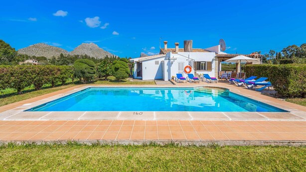 Una piscina con sillas de descanso, un flotador salvavidas y una casa con techo de tejas.
