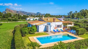 Una villa con piscina, tumbonas y vistas a las montañas.