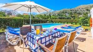 Zona de piscina con sillones de descanso, una mesa con alimentos para el desayuno y vistas a una montaña.