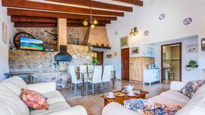 Una sala de estar acogedora con chimenea de piedra, mobiliario blanco y un comedor con mesa y sillas de vidrio.