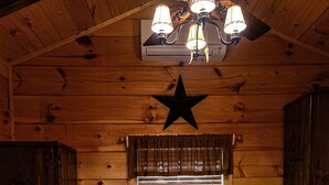 Habitación de cabaña de madera con una cama, un adorno de estrella en el techo, una ventana con persianas y un calentador.