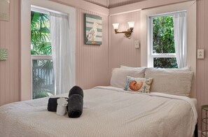 Ein Schlafzimmer mit Bett, Kissen, einer Wandleuchte und einem Fenster mit Vorhängen.
