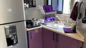 A compact kitchen with a stainless steel refrigerator, a built-in water dispenser, a dish rack with purple plates, and a window above the sink. - Perfect location (Del Valle Norte)
