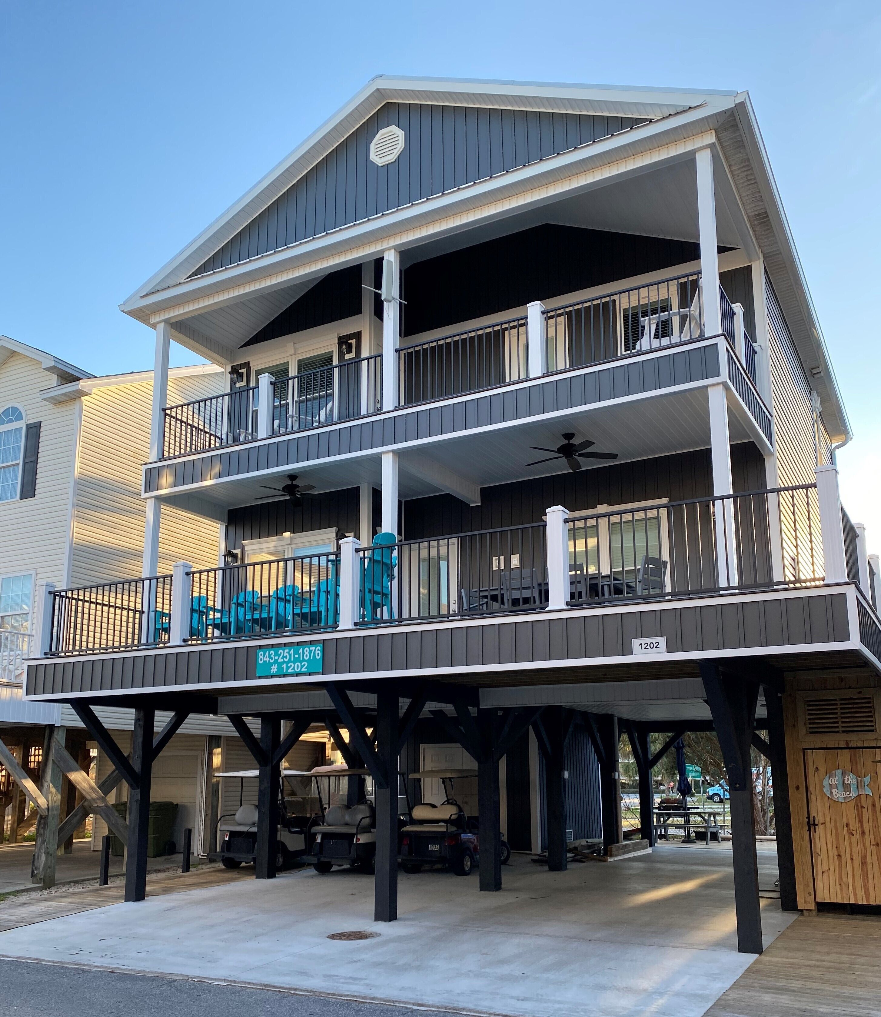 A multi-story building with a balcony on the ground floor, a covered patio area, and a sign indicating the address.