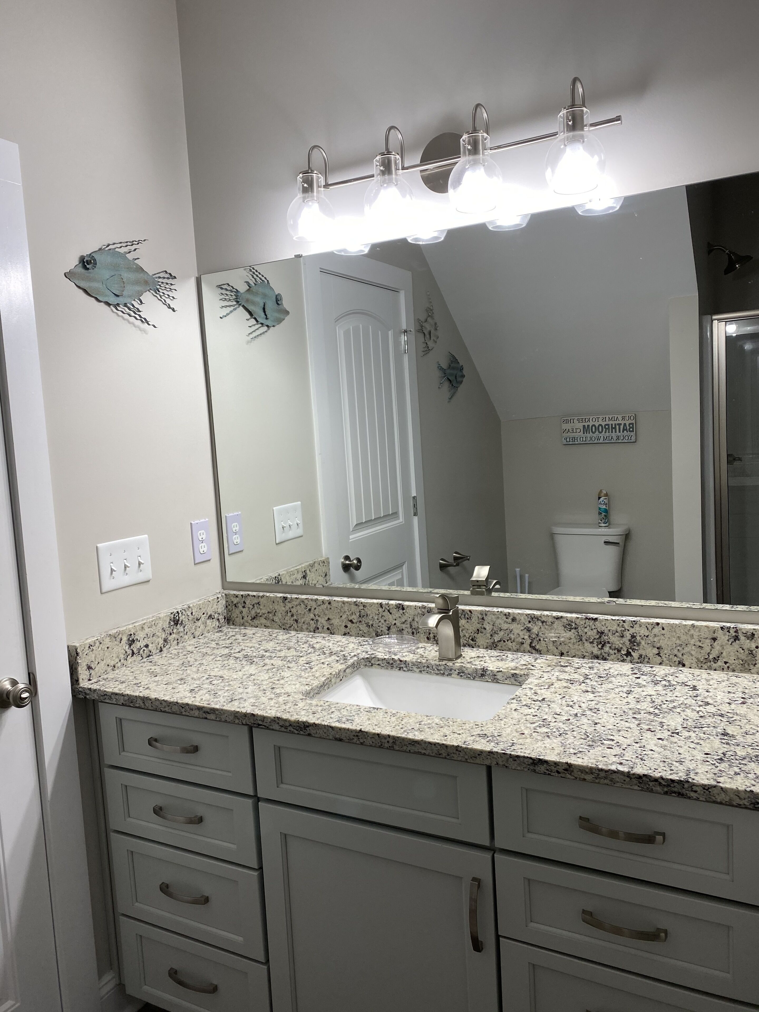 Une salle de bain avec un comptoir en granit, un lavabo, un miroir et une porte.