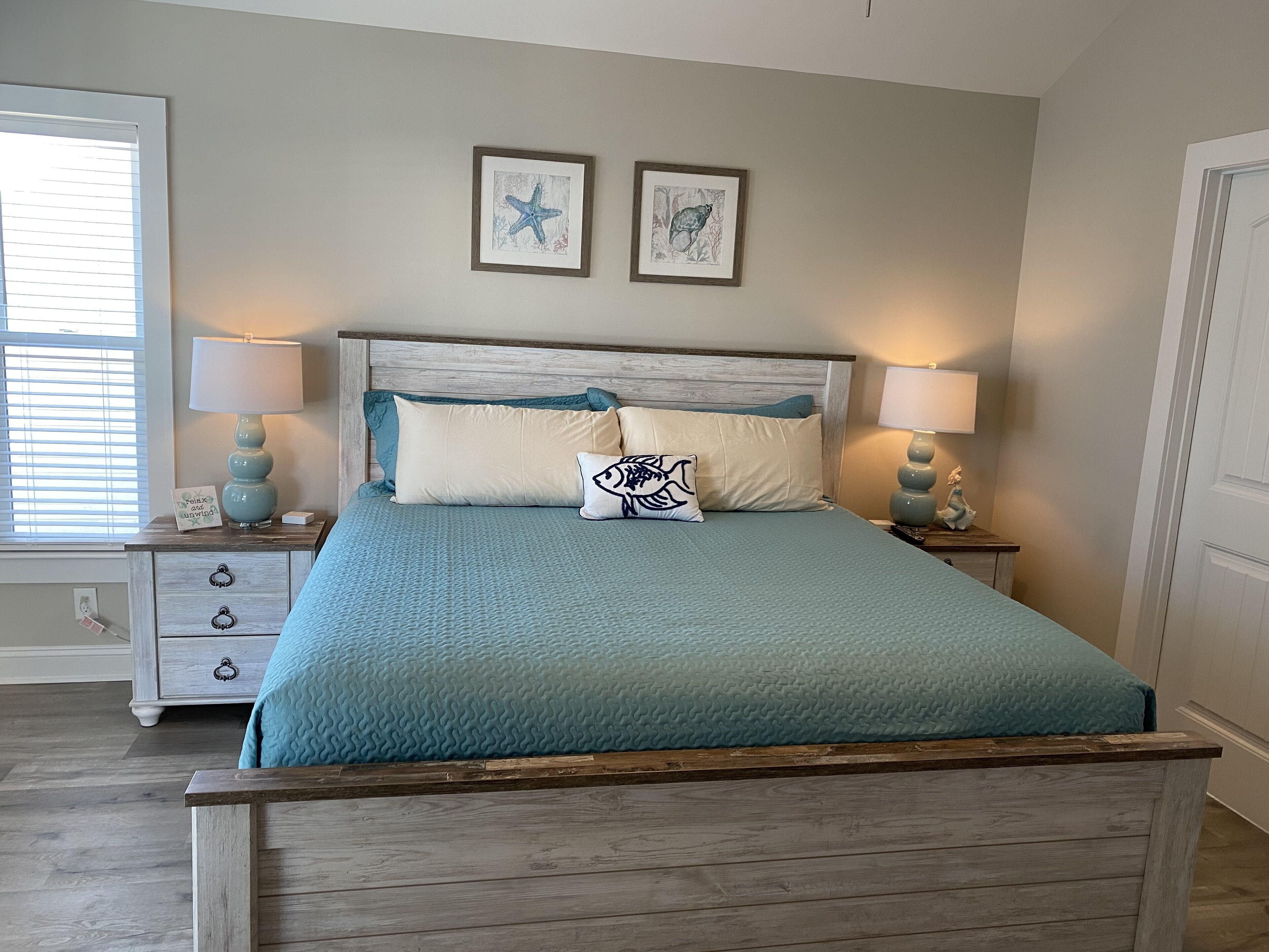 Een slaapkamer met een bed, twee nachtkastjes, een raam met zonwering en twee ingelijste foto's aan de muur.