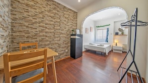 A room with a stone wall, a wooden dining table, a bed, a desk, and a clothes drying rack. - A43 - Castle Arch Apartment (Lagos)