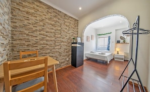 A room with a stone wall, a wooden dining table, a bed, a desk, and a clothes drying rack.