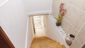 A wooden staircase leading to a room with white walls, a tiled floor, and a potted plant with pink flowers. - A43 - Castle Arch Apartment (Lagos)