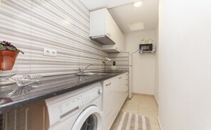Cocina compacta con lavadora, microondas y planta en maceta.