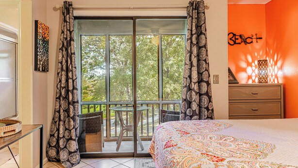 A bedroom with a large bed, a balcony with a table and chairs, and a dresser.