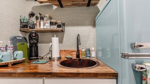A kitchen with a wooden countertop, a sink, and a shelf with kitchen utensils.