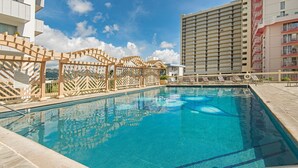 A swimming pool with a wooden deck and lounge chairs, surrounded by high-rise buildings.