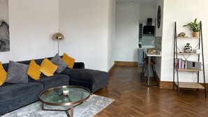 A modern living room with a dark sofa, a glass coffee table, and a kitchen in the background. - Modern 1-Bed Apartment in Chapel Allerton – Great for Longer Stays & Remote Work (Chapel Allerton)