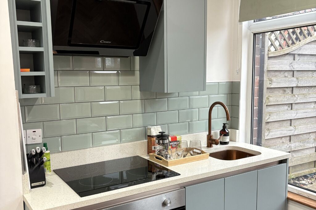A kitchen with a black induction cooktop, a stainless steel sink, and a wooden tray with kitchen items.