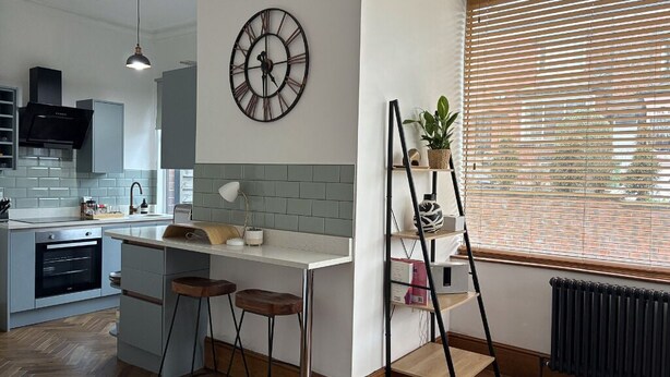 A modern kitchen with a built-in island, bar stools, a clock, and a radiator. - Modern 1-Bed Apartment in Chapel Allerton – Great for Longer Stays & Remote Work (Chapel Allerton)