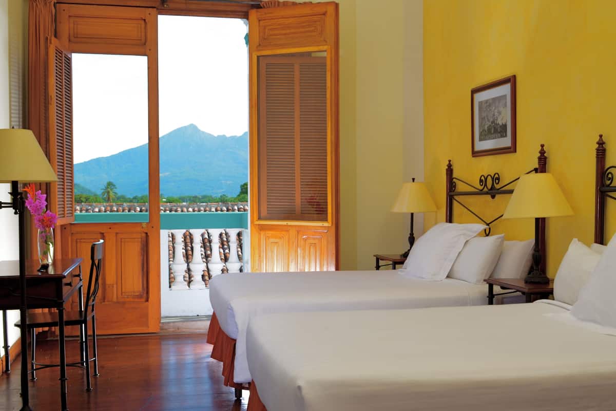 A hotel room with two beds, a desk with a chair, and a view of a mountain and water.