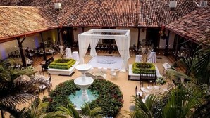 Salón de bodas al aire libre con pista de baile techada, mesas y una fuente.