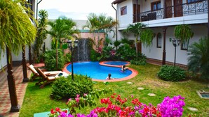 Un patio con piscina, sillas de descanso y una cascada.