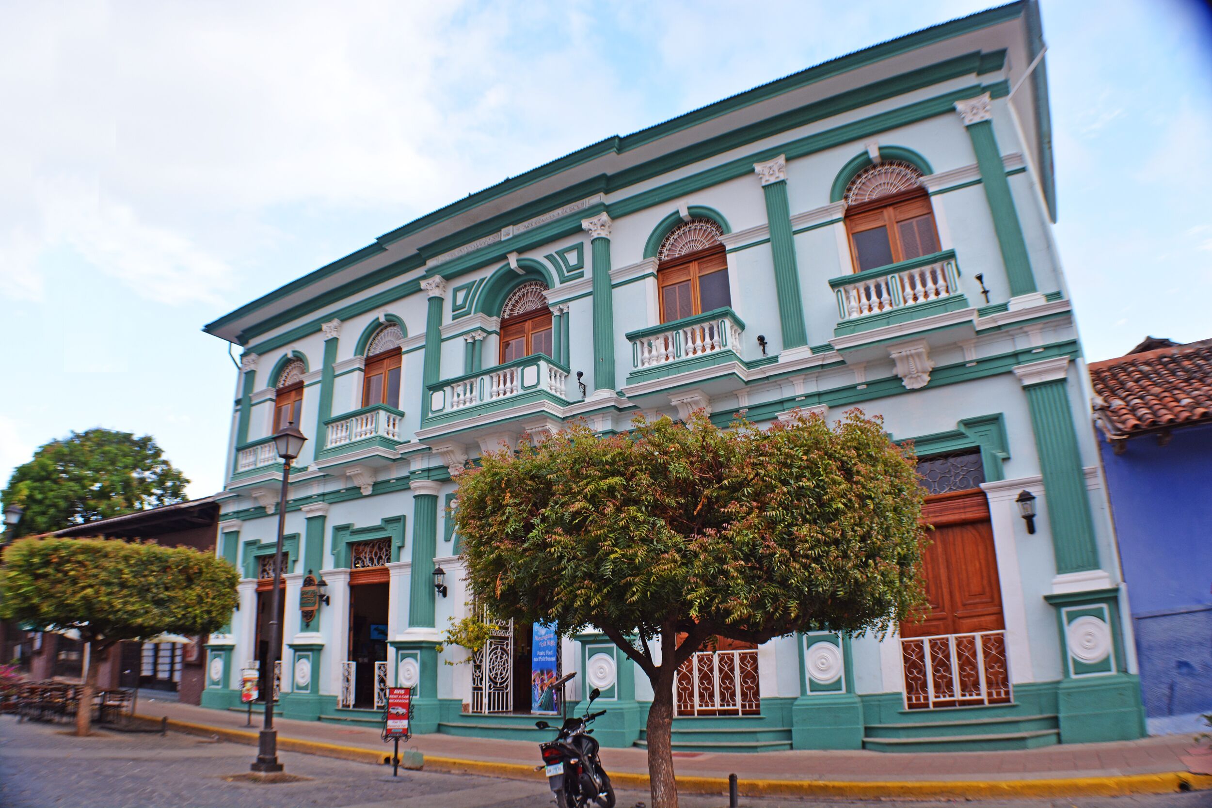 Un edificio histórico con fachada verde y blanca, varios balcones y un árbol en primer plano.
