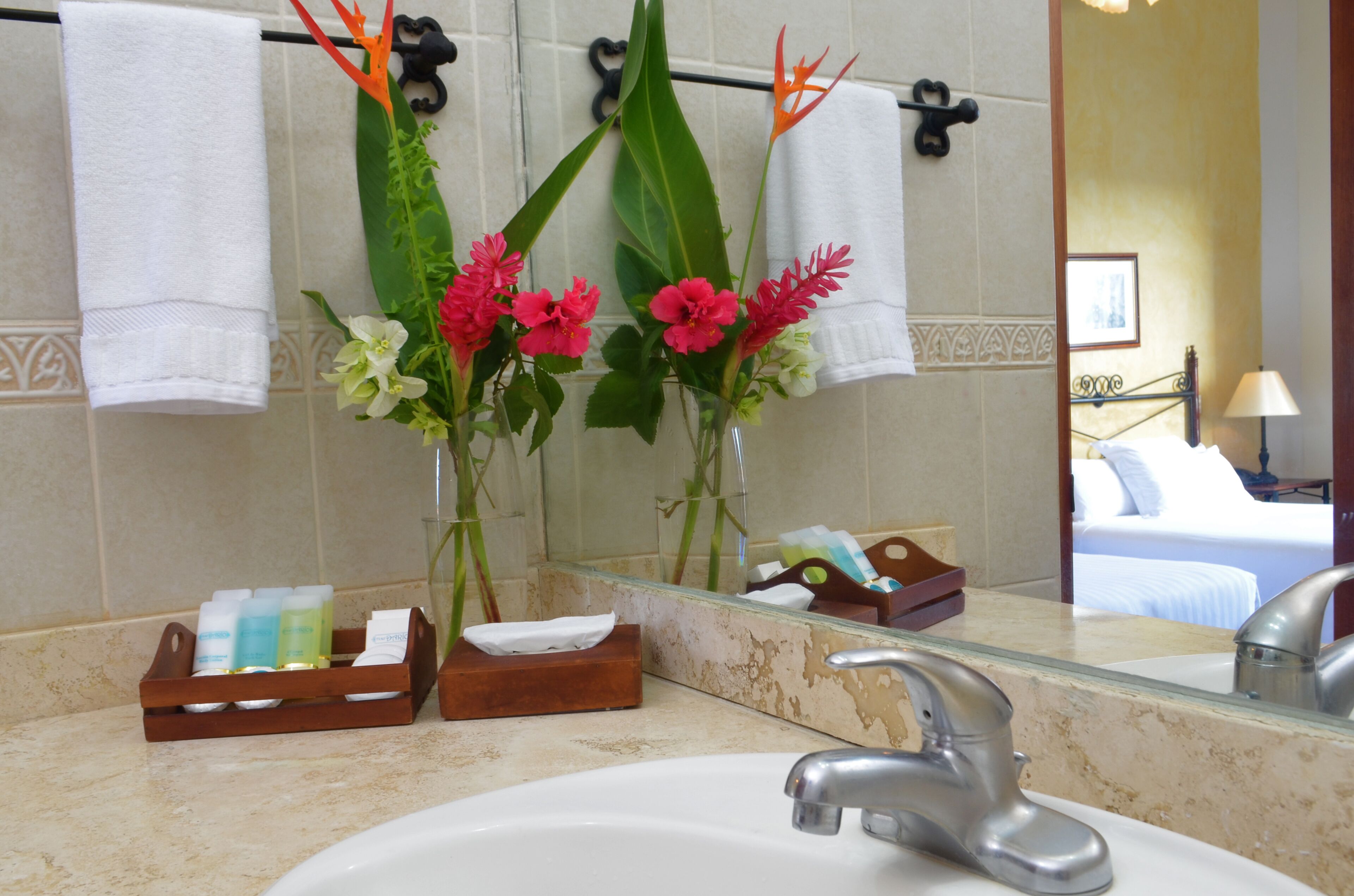 A bathroom with a sink, mirror, and towels. There are flowers in a vase on the counter.