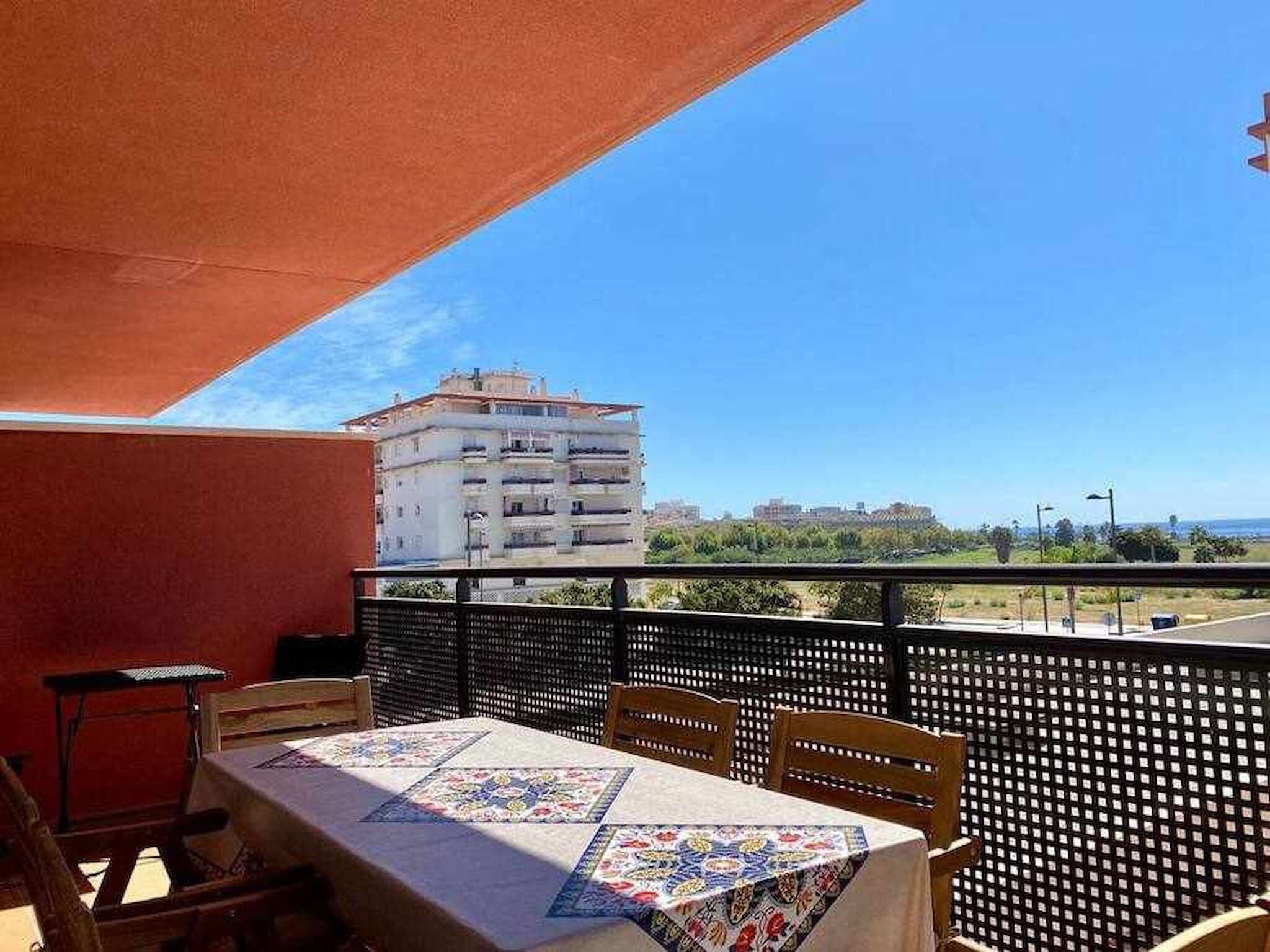 A balcony with a table and chairs, a view of a building, and a clear sky.