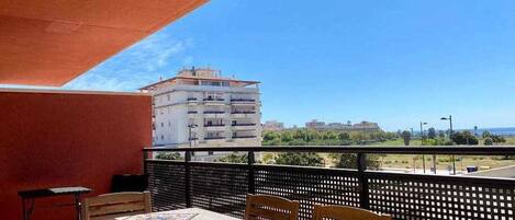 A balcony with a table and chairs, a view of a building, and a clear sky.