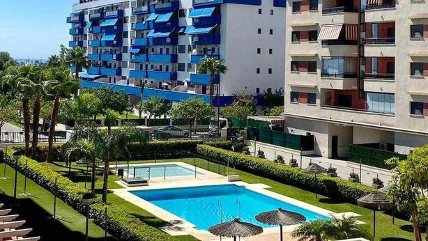 Ein Hotel mit Schwimmbad, umgeben von gepflegten Gärten und Palmen.