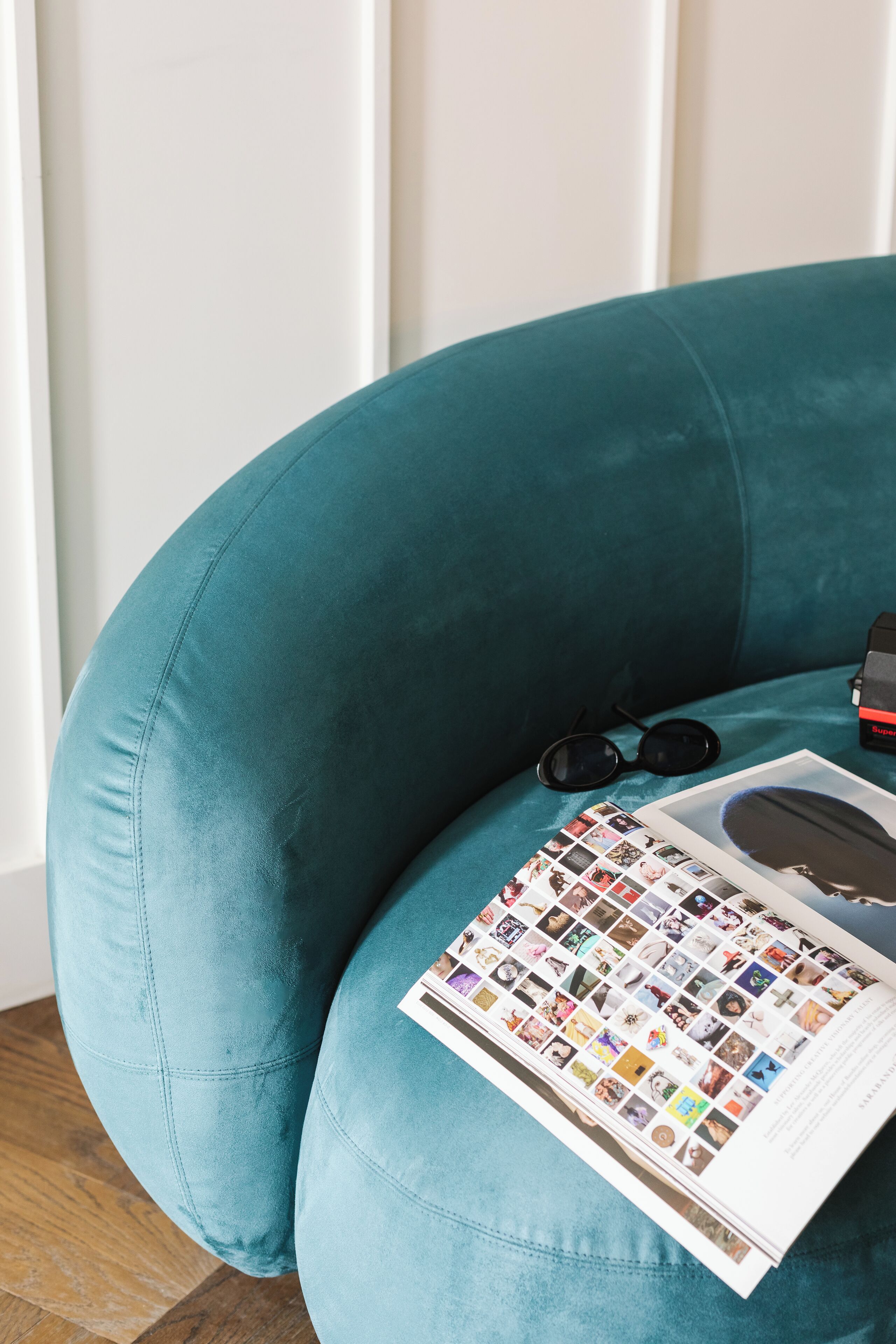A teal armchair with a magazine and sunglasses on it.