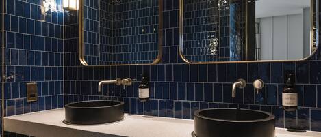 A bathroom with two black sinks, a mirror, and a wall with blue tiles.