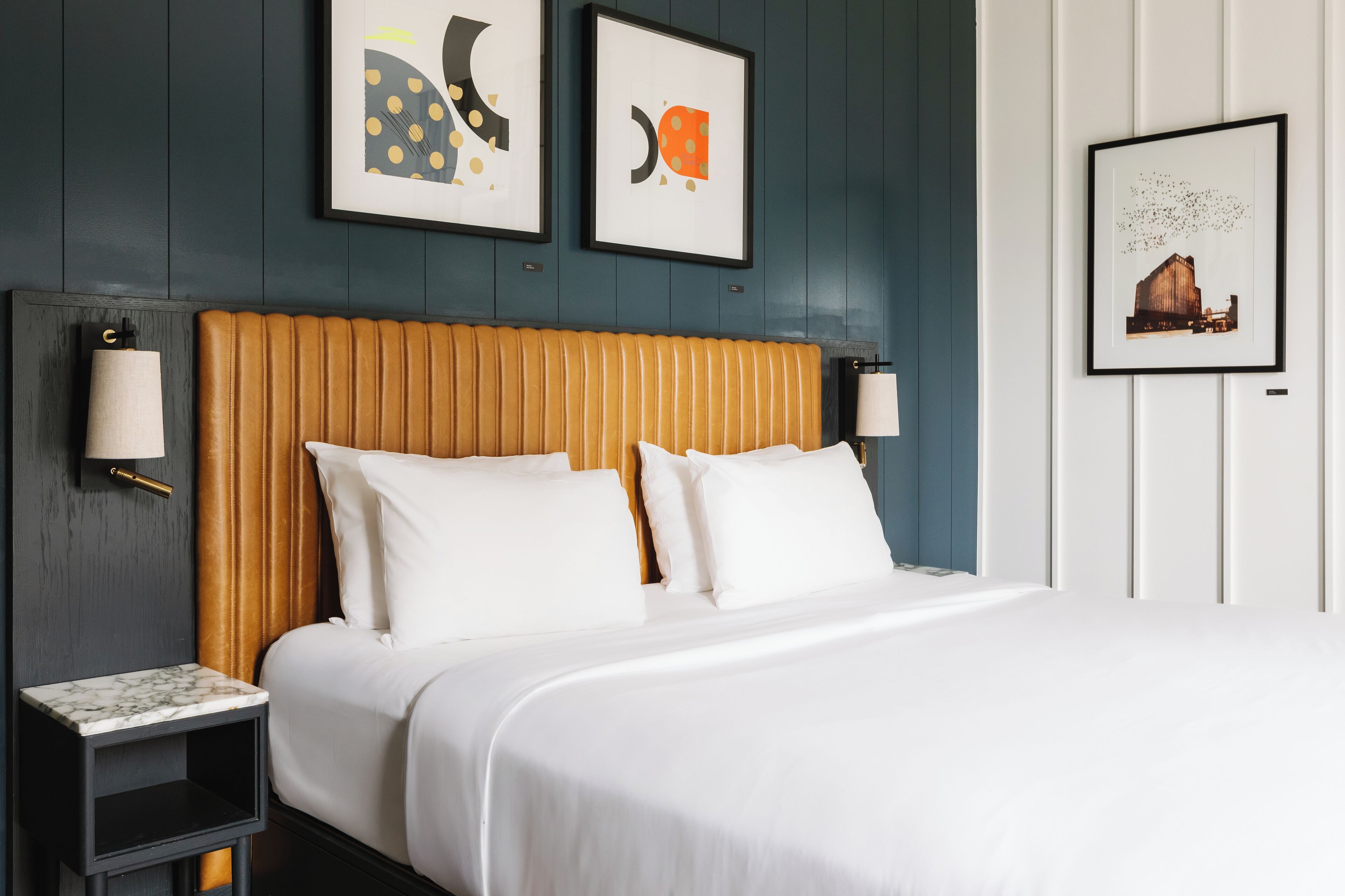 A hotel room with a large bed, two bedside tables, and artwork on the walls.