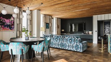 Una sala moderna con techo de madera, una mesa redonda de comedor con sillas, un sofá y una zona de cocina con televisión.